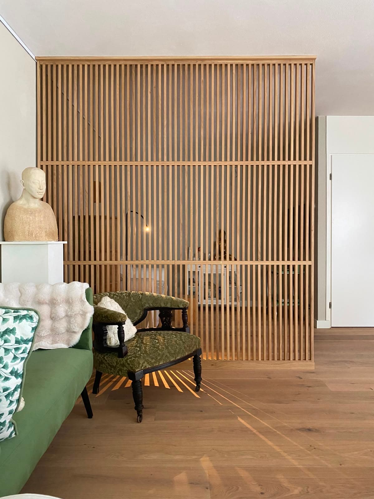Moderne houten roomdivider met verticale latten van massief eikenhout als scheidingswand in een woonkamer interieur.