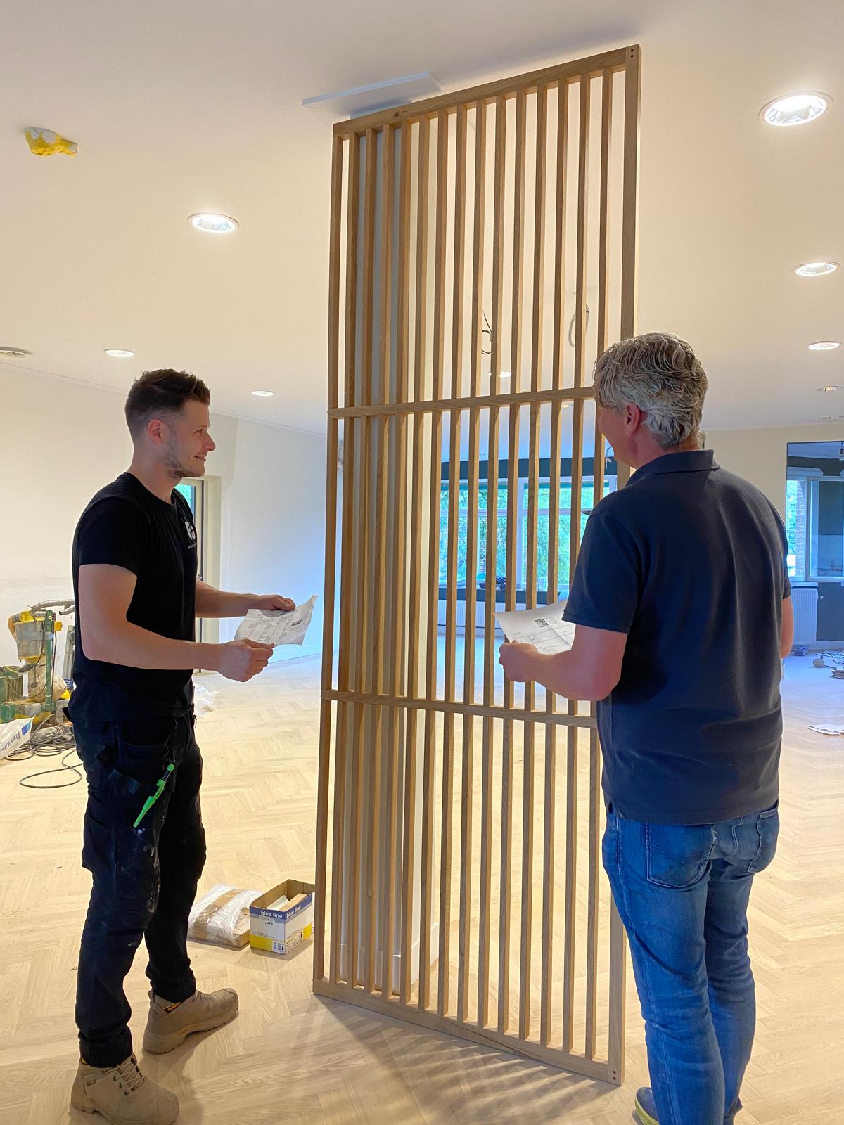 Installatie van een houten roomdivider met latten in een woonkamer
