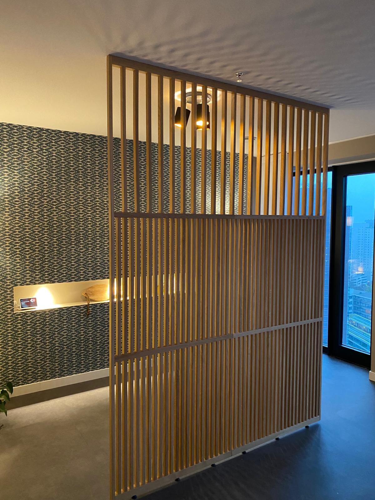 Zijaanzicht van de Model Light® roomdivider in RAL 7021 zwart. Het open ontwerp zorgt voor een modern lichtspel. Foto toont de blank eiken uitvoering ter illustratie van het design