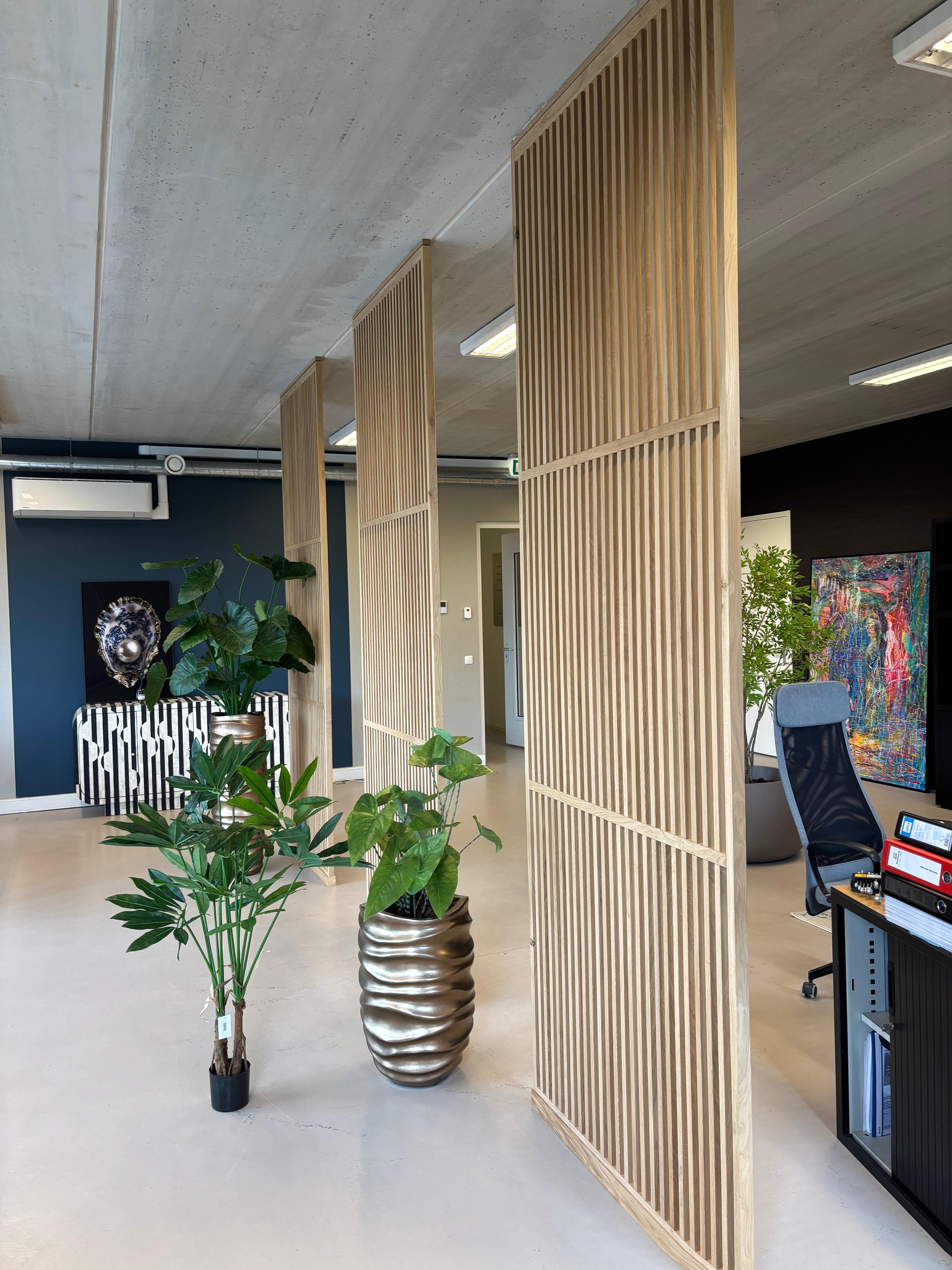 Kamerhoge houten roomdivider onder een beton plafond in moderne kantoorruimte met massief eiken latten