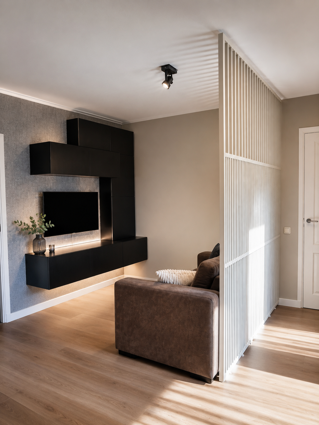 Plafondhoge roomdivider naast de bank in RAL 9010 wit met open bovenstructuur, waardoor de zithoek wordt gescheiden terwijl licht en zicht behouden blijven.